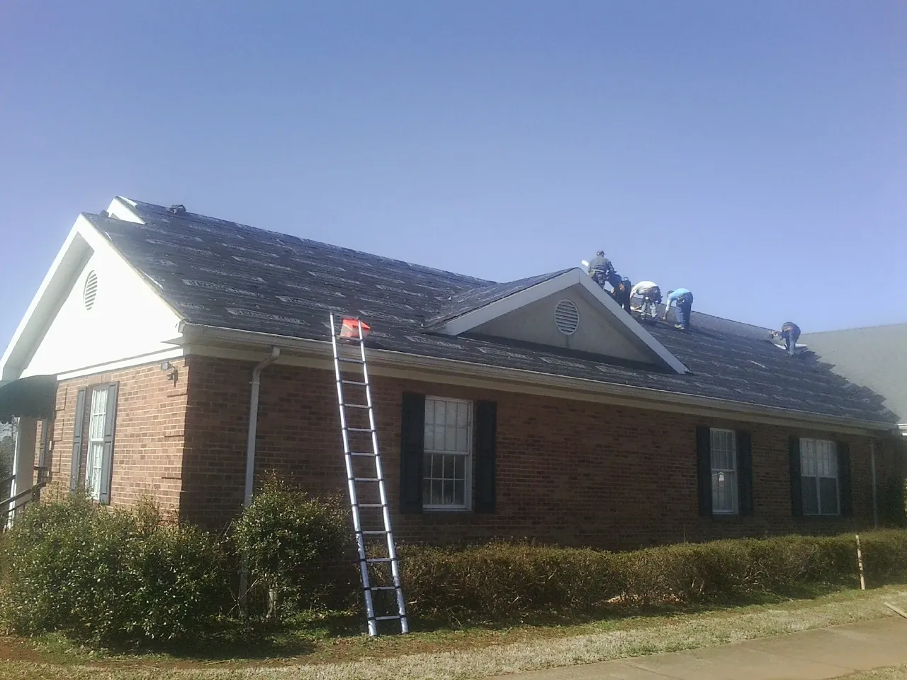 Crew tearing shingles off a brick ranch roof with a ladder set — Emergency Roof Repair work by our crew in Candler