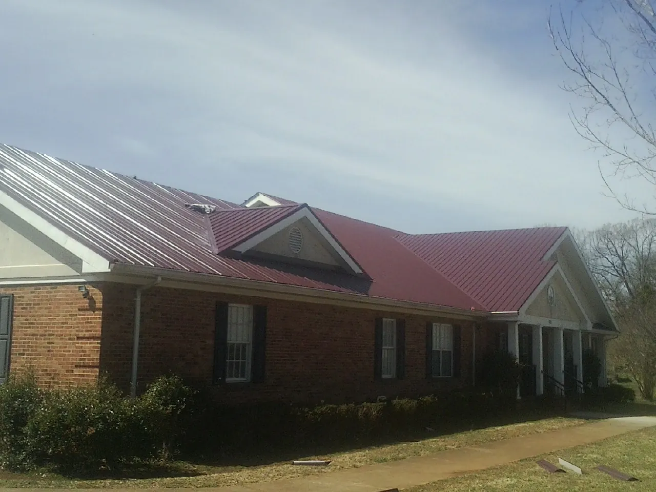 Red metal roof with gabled entries on a long brick building, from a Hail Damage Roof Repair job in Candler