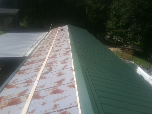 Old rusted panels beside newly installed green metal roofing — Wind Damage Roof Repair by Roofing Brothers in Candler