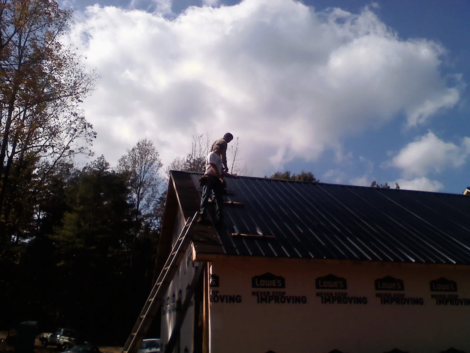 Roofer fastening dark metal panels high against a cloudy sky, from a Roof Inspection job in Candler