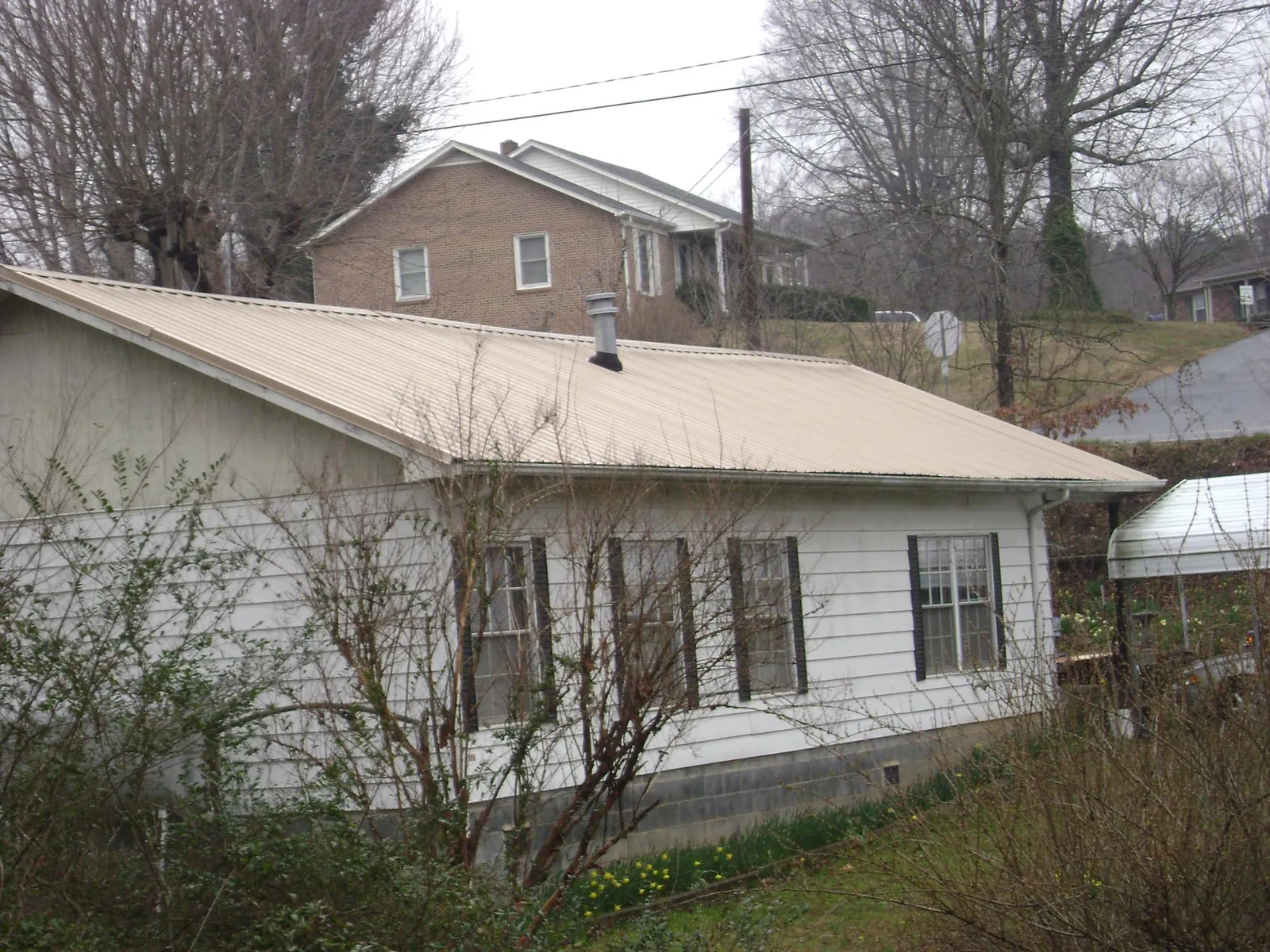 Tan metal roof on a white sided house set into a hillside — Commercial Roofing by Roofing Brothers in Candler