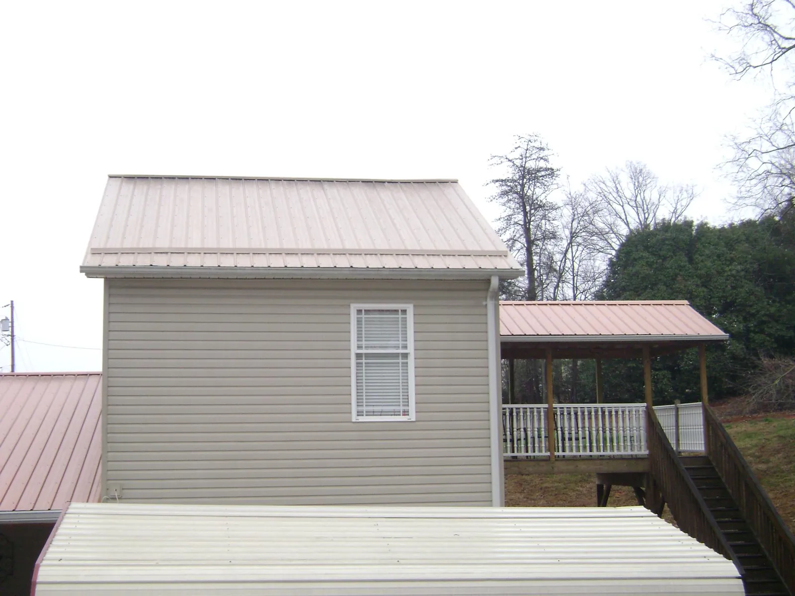 Tan metal roofs on a two story addition and attached porch, from a Roof Replacement job in Candler